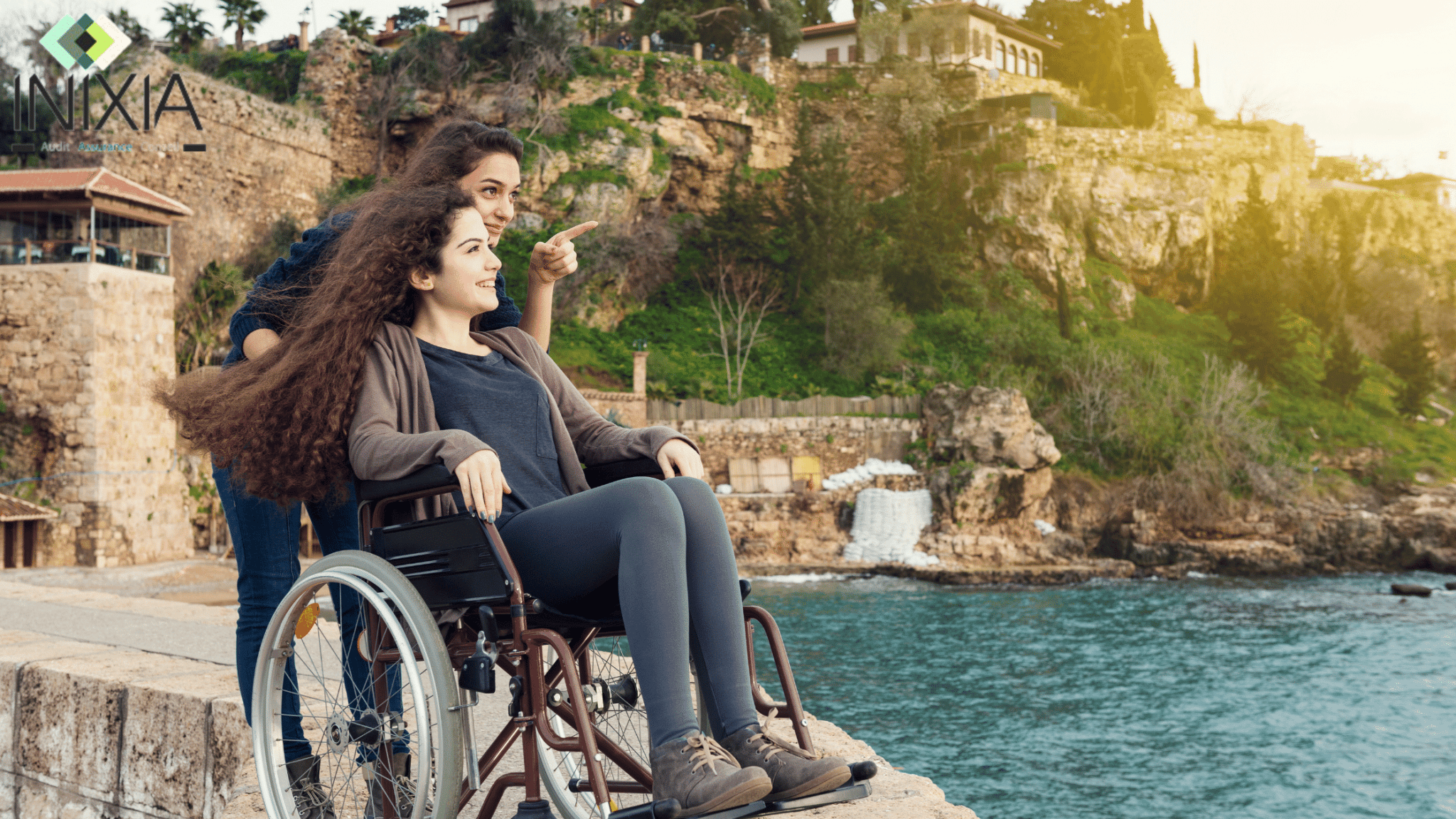 Une femme handicapée sur une chaise roulante est poussée par une amie. Les deux femmes ont le sourire en regardant la mer.