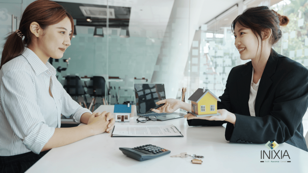 Deux femmes discutant des options d'assurance habitation avec des maquettes de maisons sur la table dans un bureau, illustrant un service de conseil professionnel. -INIXIA