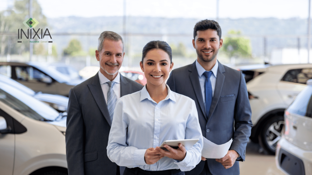 Trois professionnels de l'assurance automobile souriants, deux hommes et une femme, debout dans une salle d'exposition de voitures, avec un logo INIXIA en arrière-plan.
