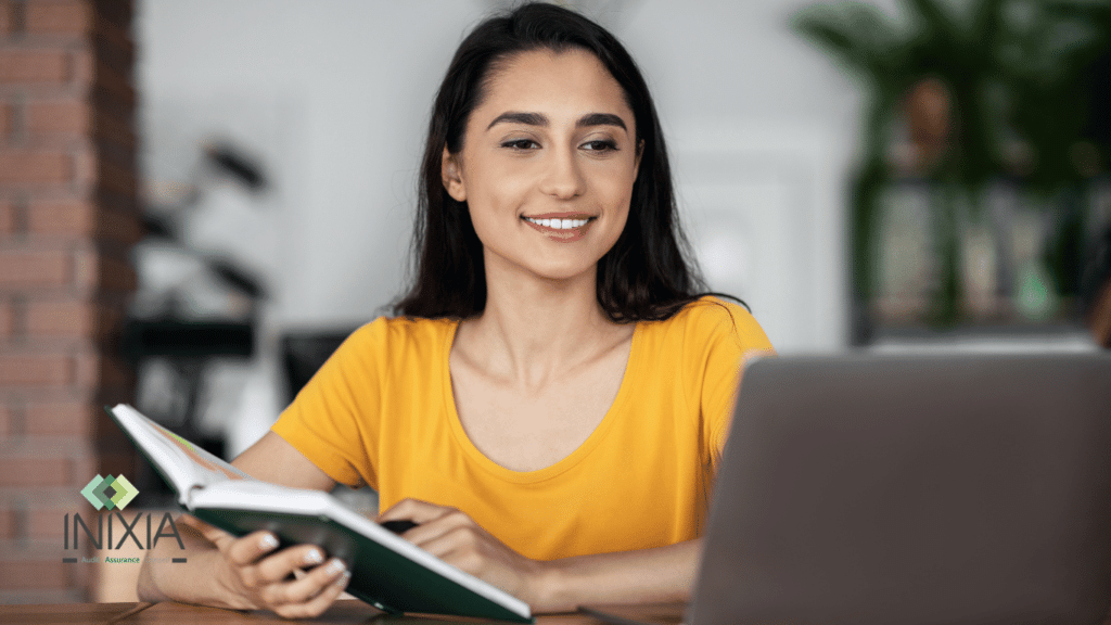 Une jeune femme professionnelle en tenue décontractée jaune sourit tout en consultant un agenda et en travaillant sur son ordinateur portable, avec le logo d'INIXIA, spécialiste en audit, assurance et conseil, en arrière-plan.