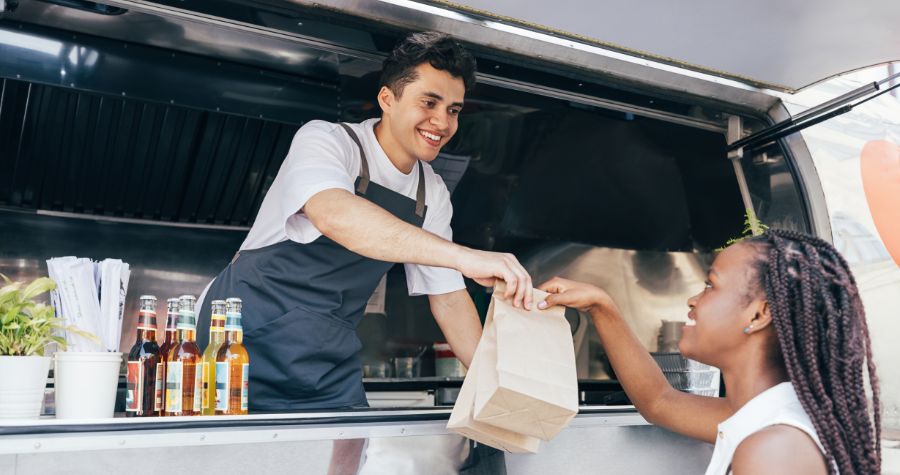 un restaurant dans son food truck, en train de donner une commande à sa cliente